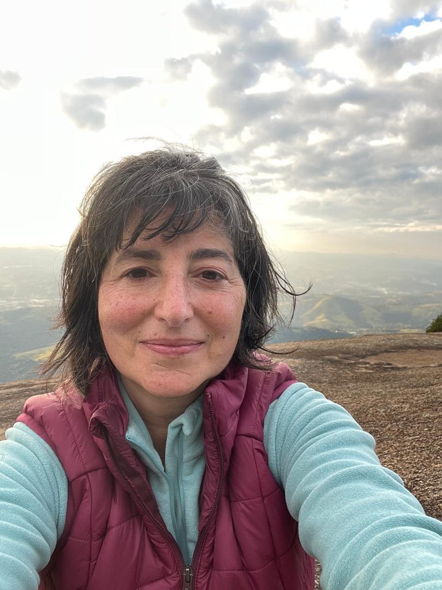 Fabiana Dupont sorrindo no alto de uma montanha, com o vale ao fundo